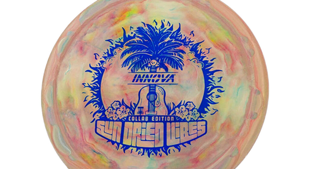Innova Test-Pro Pig (Sun Dried Vibes) Galaxy color disc (beige, orange-ish, green) w/Blue Stamp. The image shown on the disc has summery atmosphere with its inclusion of coconut trees, Hibiscus flowers, and a guitar, evoking a tropical and musical ambiance.